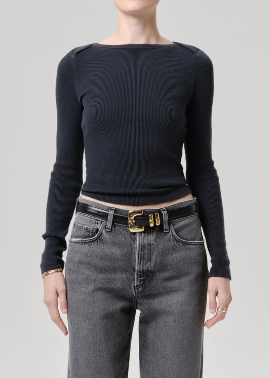 Person wearing a black long-sleeve top and gray jeans with a gold belt on a grey background