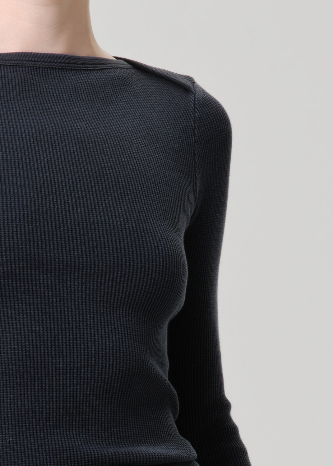 Black long-sleeve top worn by a person on a grey background