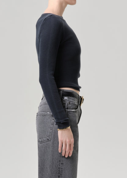 Person wearing a black long-sleeve top and gray jeans on a grey background