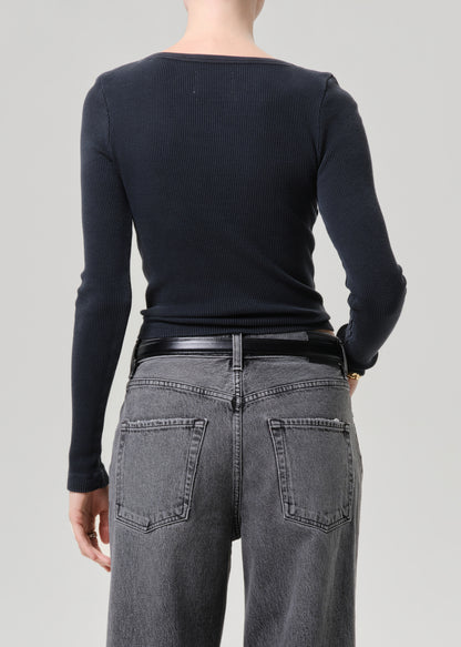 Person wearing a black long-sleeve top and gray jeans on a grey  background