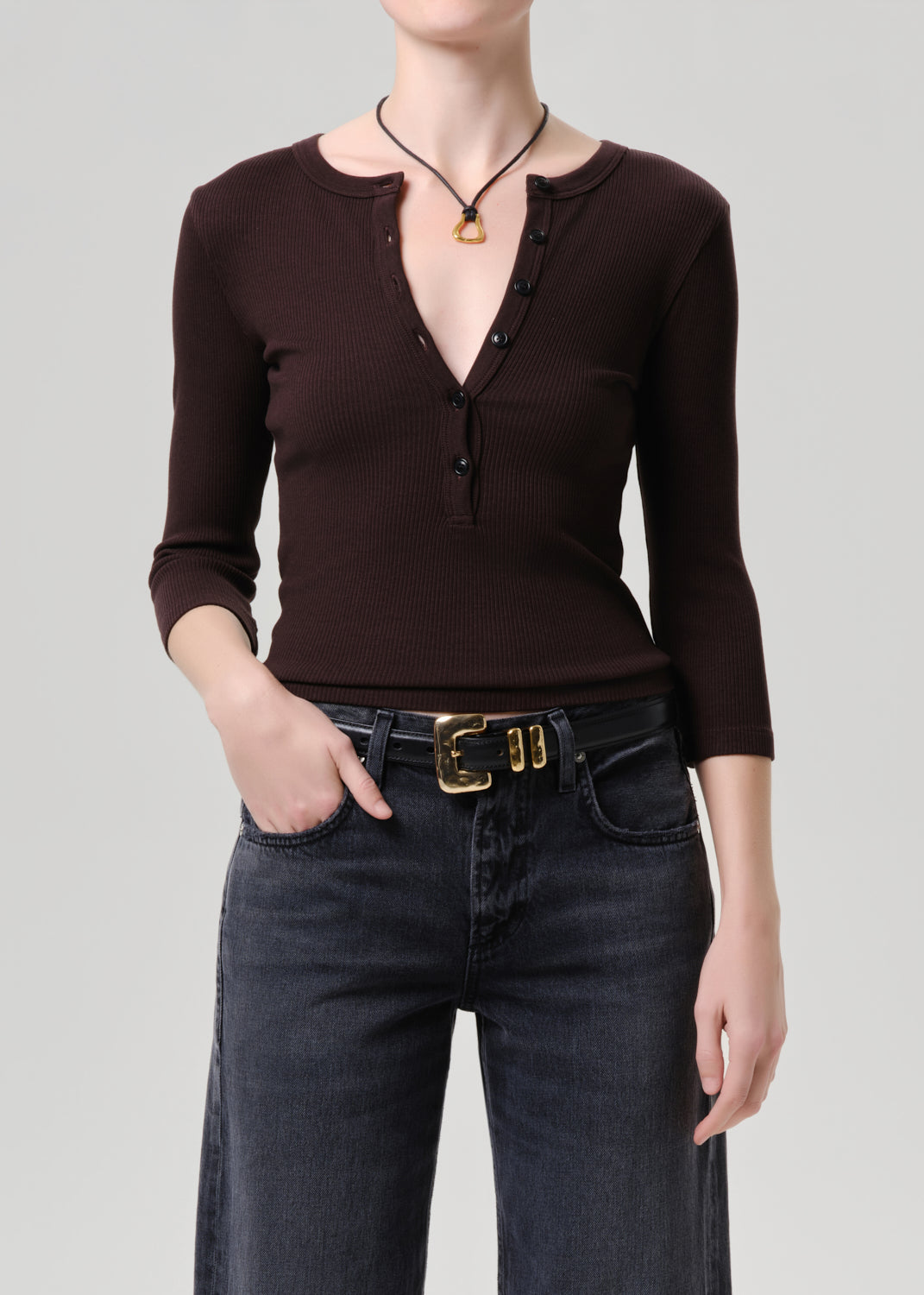 Person wearing a brown long-sleeve top and dark jeans on a grey background