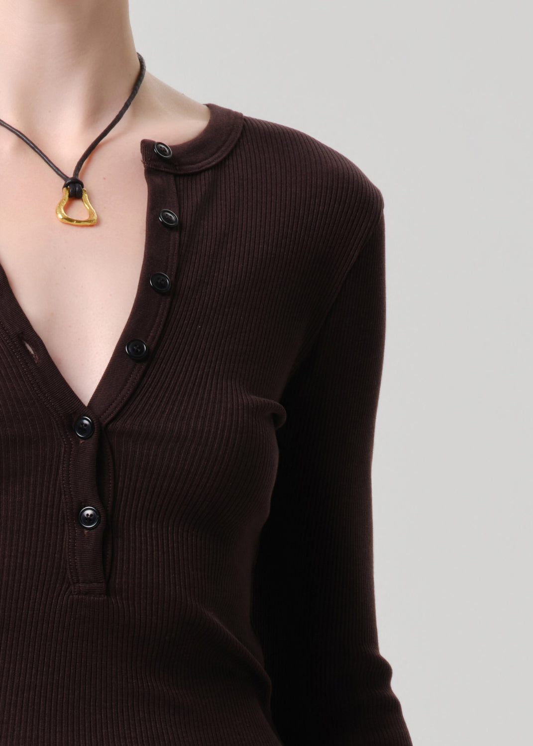 Brown ribbed sweater with buttons and a necklace on a grey background