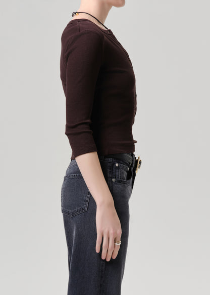 Person wearing a brown hoodie and dark jeans on a grey background