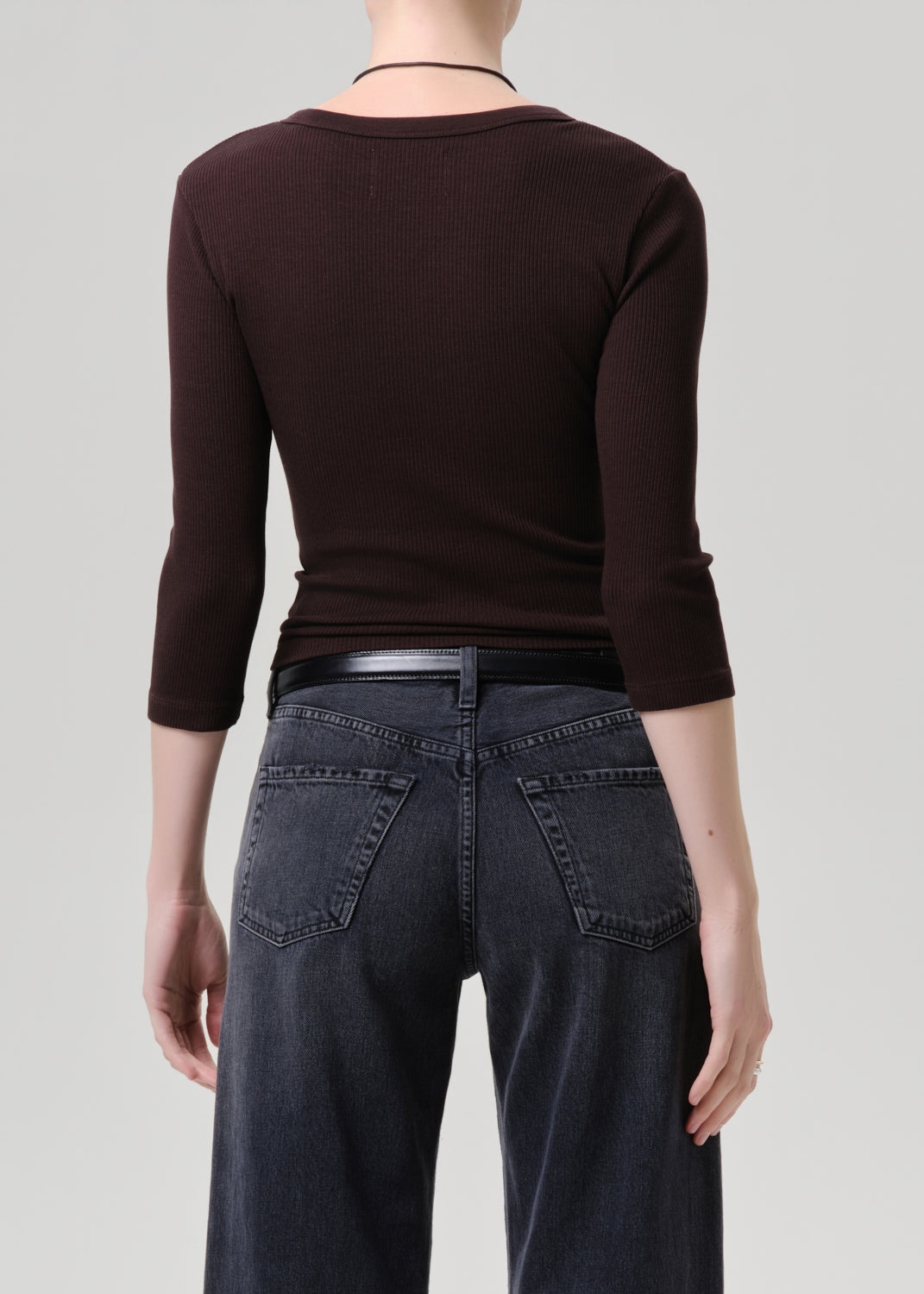 Back of person wearing a brown long-sleeve top and dark jeans on a grey background