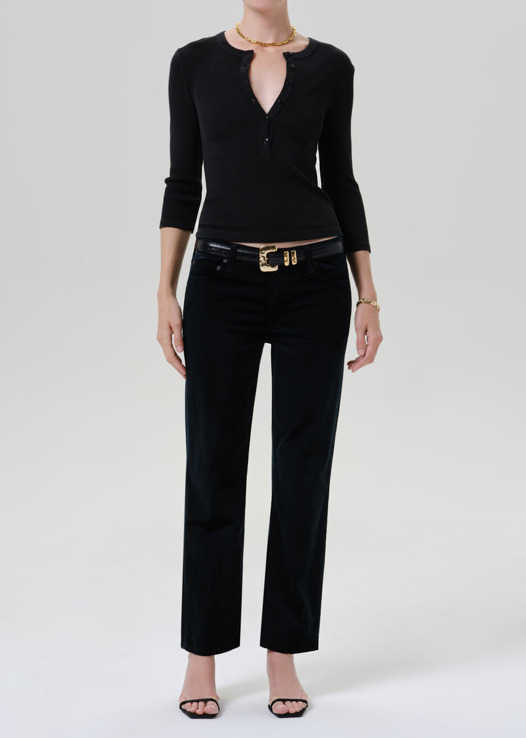 Person wearing a black long sleeve henley top with black pants and black sandals on a grey background