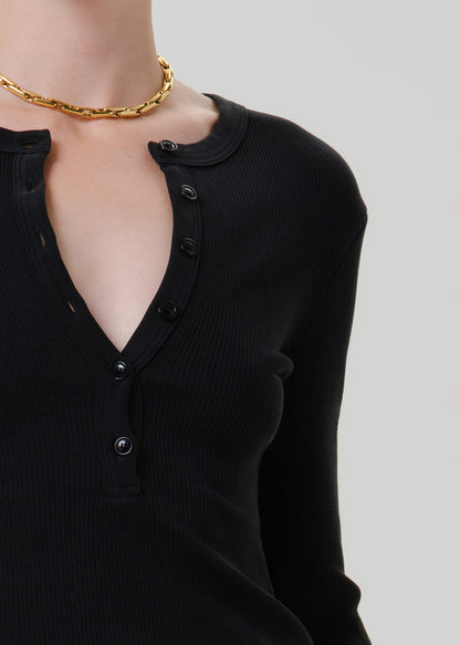 Person wearing a black long sleeve henley top on a grey background