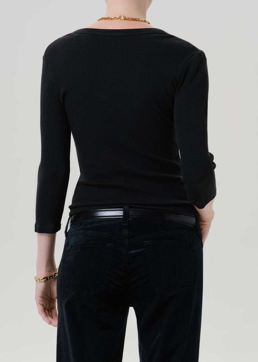 Person wearing a black long sleeve henley top with black pants viewed from the back on a grey background