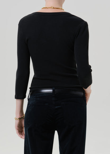Person wearing a black long sleeve henley top with black pants viewed from the back on a grey background