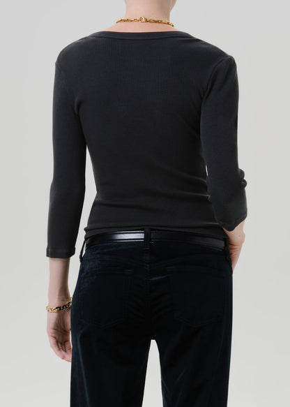 Person wearing a black long sleeve fitted henley top with black jeans, back cropped view on a grey background.