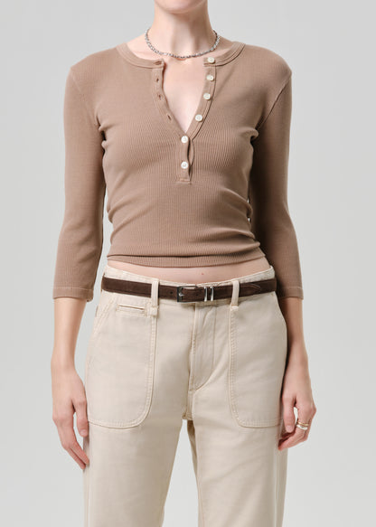 Person wearing a brown long-sleeve top with buttons and beige pants on a grey background