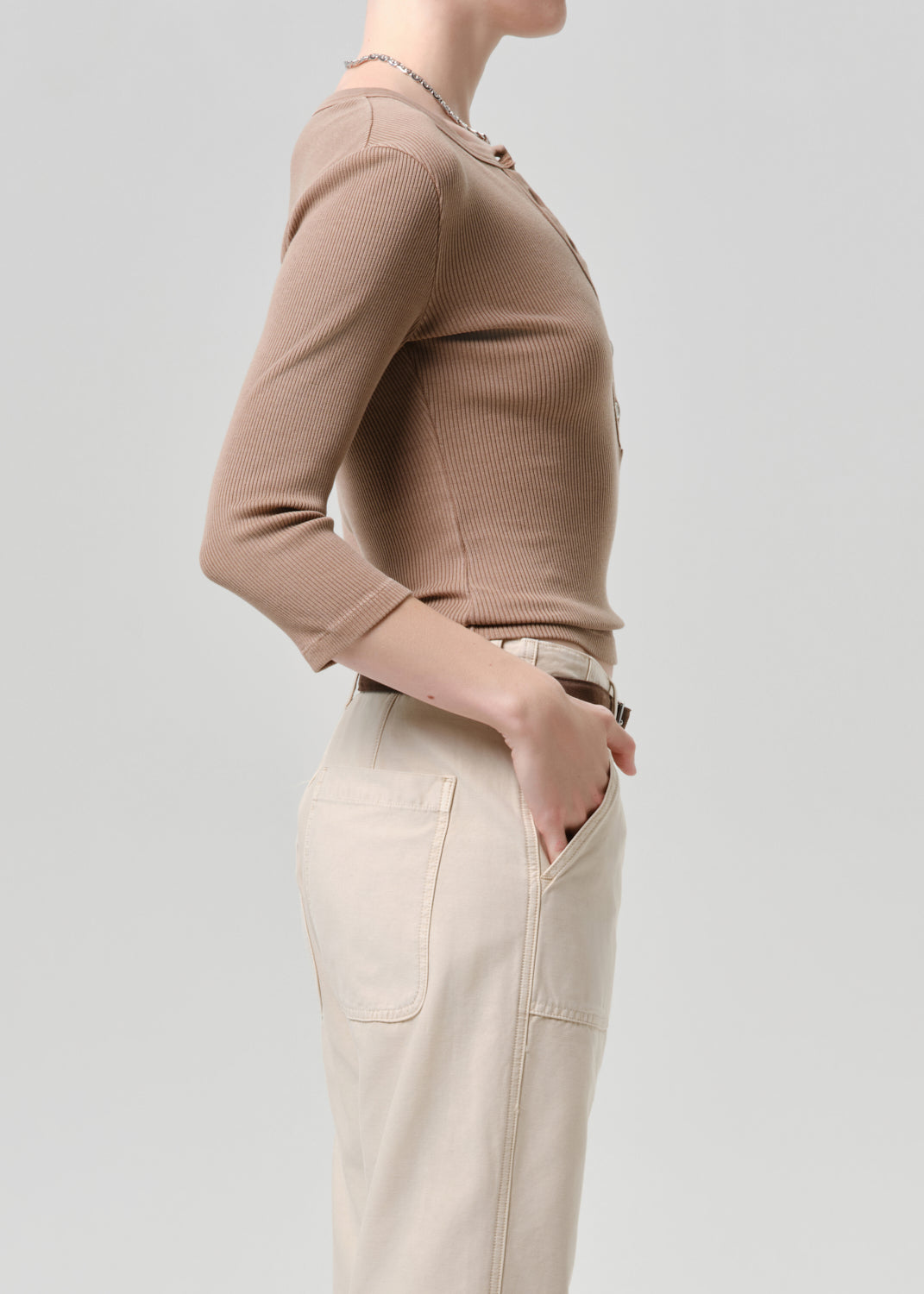 Person wearing a beige sweater and pants on a grey background