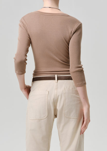 Person wearing a brown ribbed long-sleeve top and beige pants on a grey background