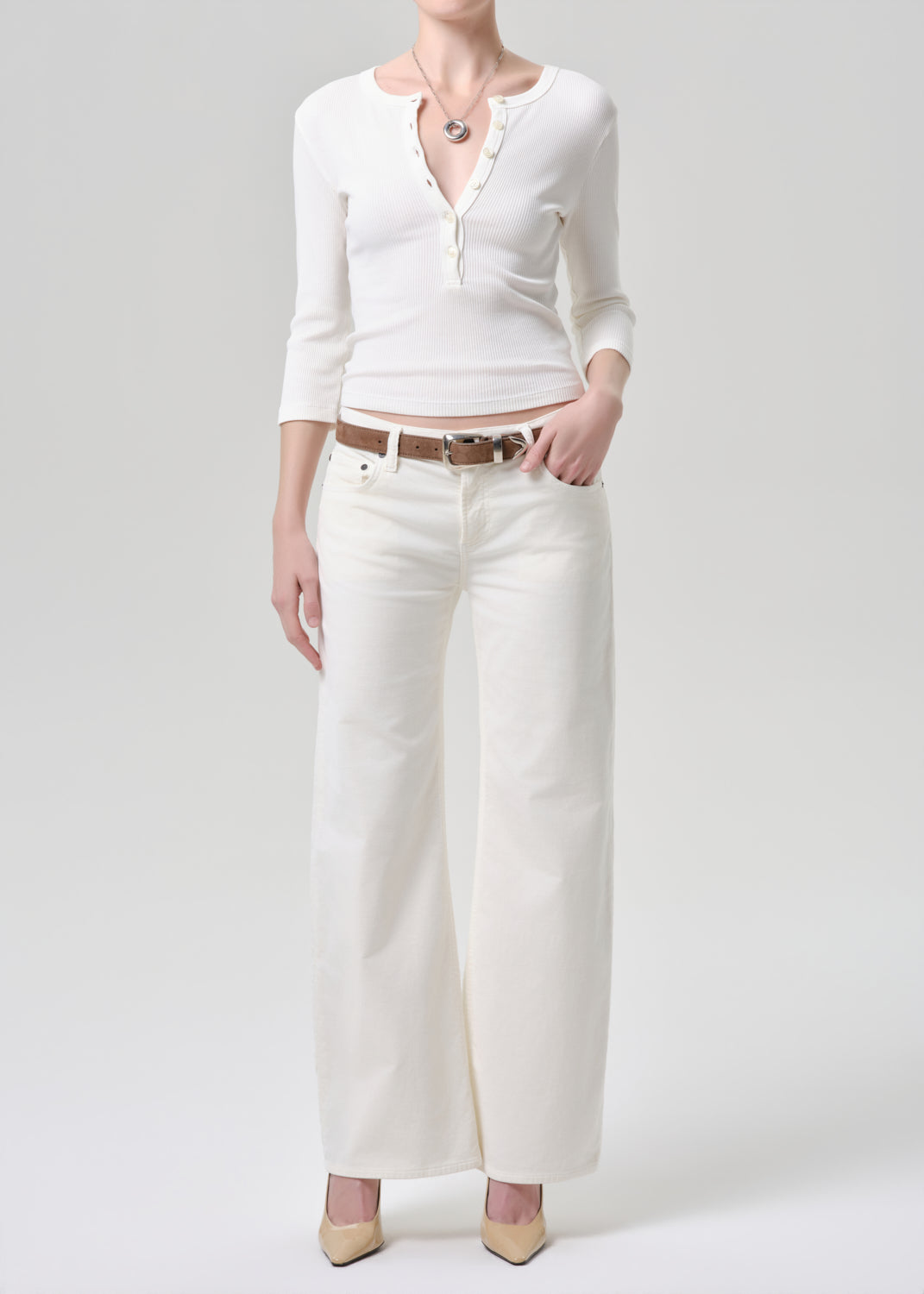 Person wearing a white cardigan, white pants, and beige shoes on a grey background