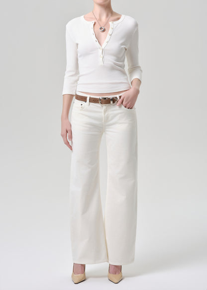 Person wearing a white cardigan, white pants, and beige shoes on a grey background