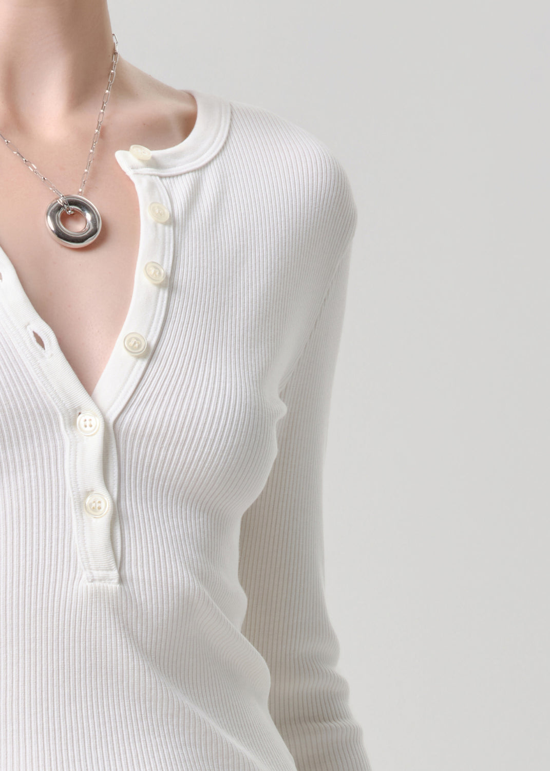 White long-sleeve shirt with buttons and a necklace on a grey background