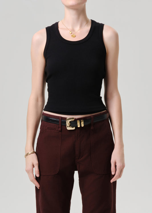 Person wearing a black sleeveless top and maroon pants with a gold belt on a grey background