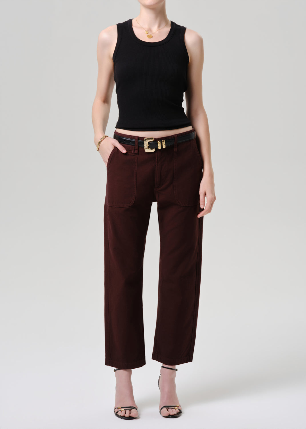 Person wearing a black sleeveless top and brown pants on a grey background