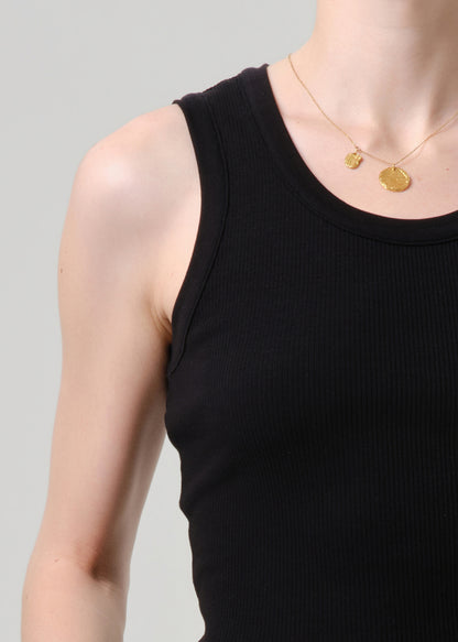 Person wearing a black tank top with gold necklaces on a grey background