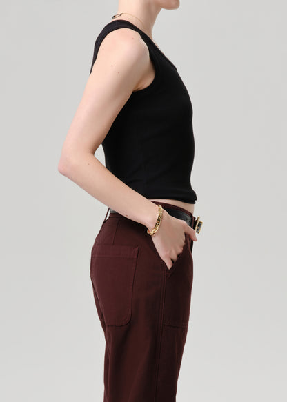 Person wearing a black sleeveless top and brown pants on a grey background