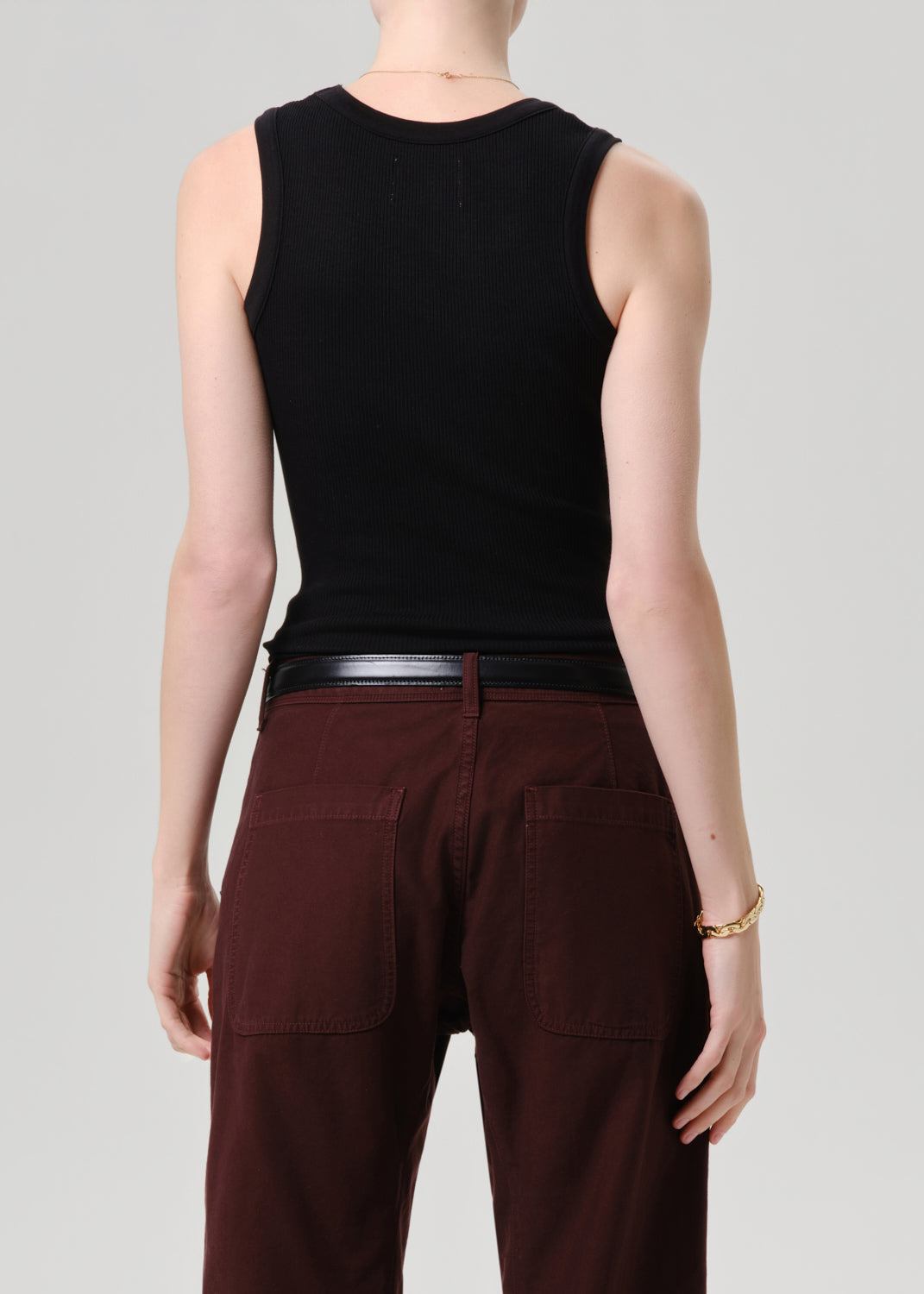 Person wearing a black sleeveless top and brown pants on a grey background