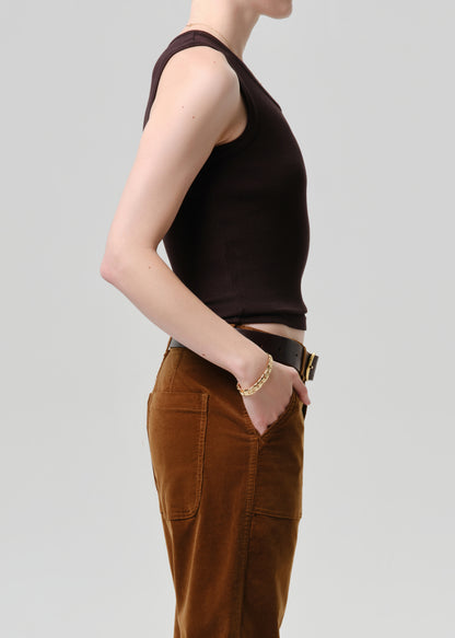 Person wearing a brown sleeveless top and brown pants on a grey background