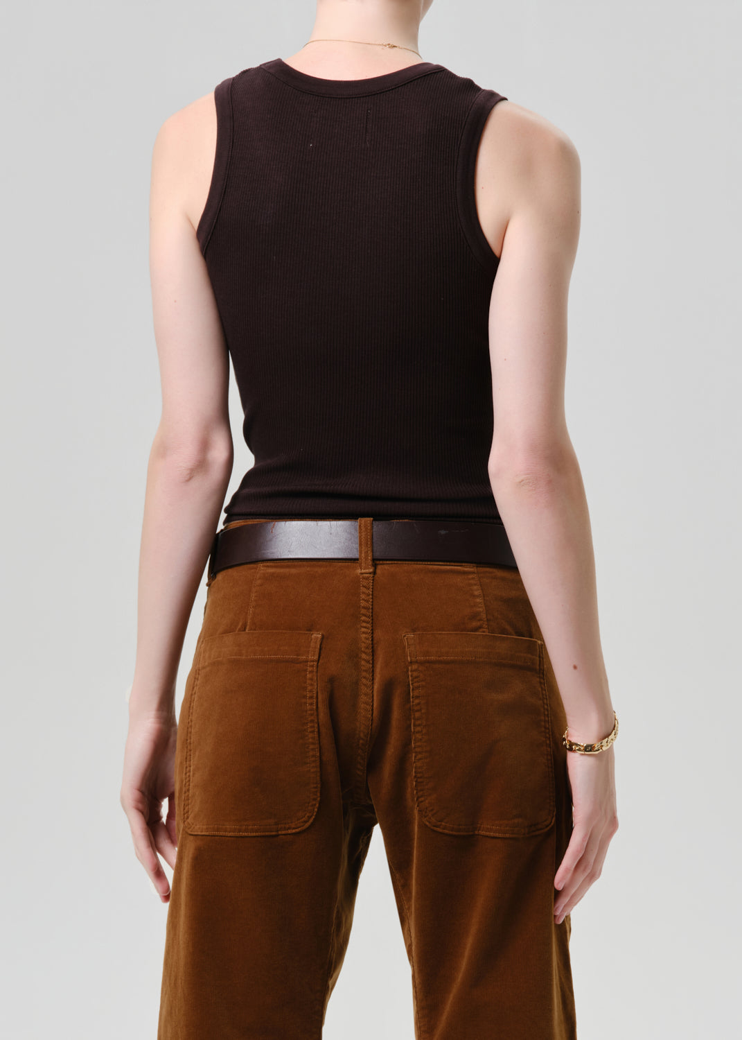 Person wearing a black sleeveless top and brown pants on a grey background