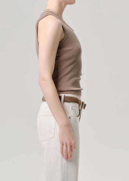 Person wearing a brown sleeveless top and light-colored pants on a grey background