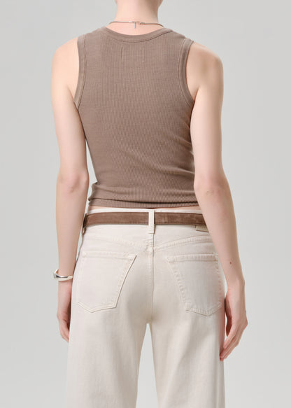 Person wearing a brown ribbed tank top and beige pants on a grey background