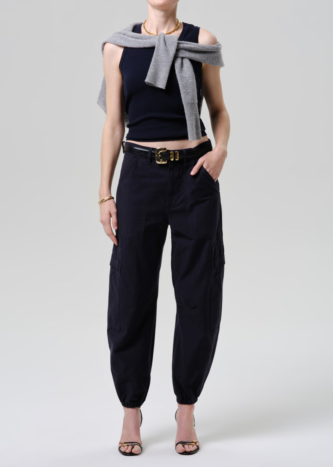 Person wearing a black sleeveless top, black pants, and a gray scarf on a grey background