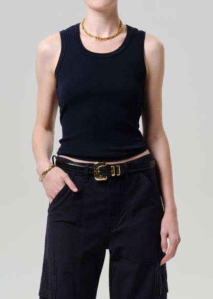 Person wearing a black sleeveless top and black pants with a gold belt on a grey background