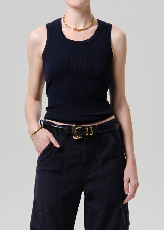 Person wearing a black sleeveless top and black pants with a gold belt on a grey background