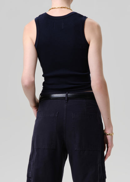 Person wearing a black sleeveless top and dark pants on a grey background