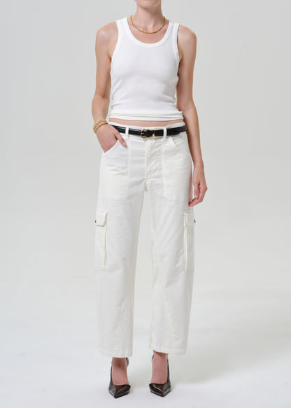 A model wearing a white ribbed tank top, white cropped cargo pants with a black belt, and black heels, standing against a light gray studio background.