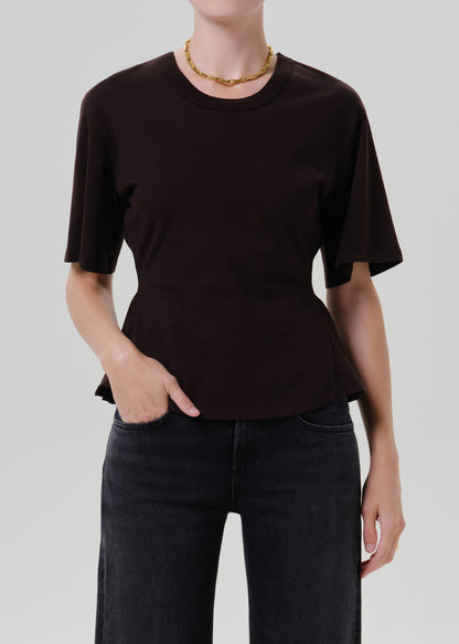Person wearing a dark brown short sleeve crewneck top on a grey background