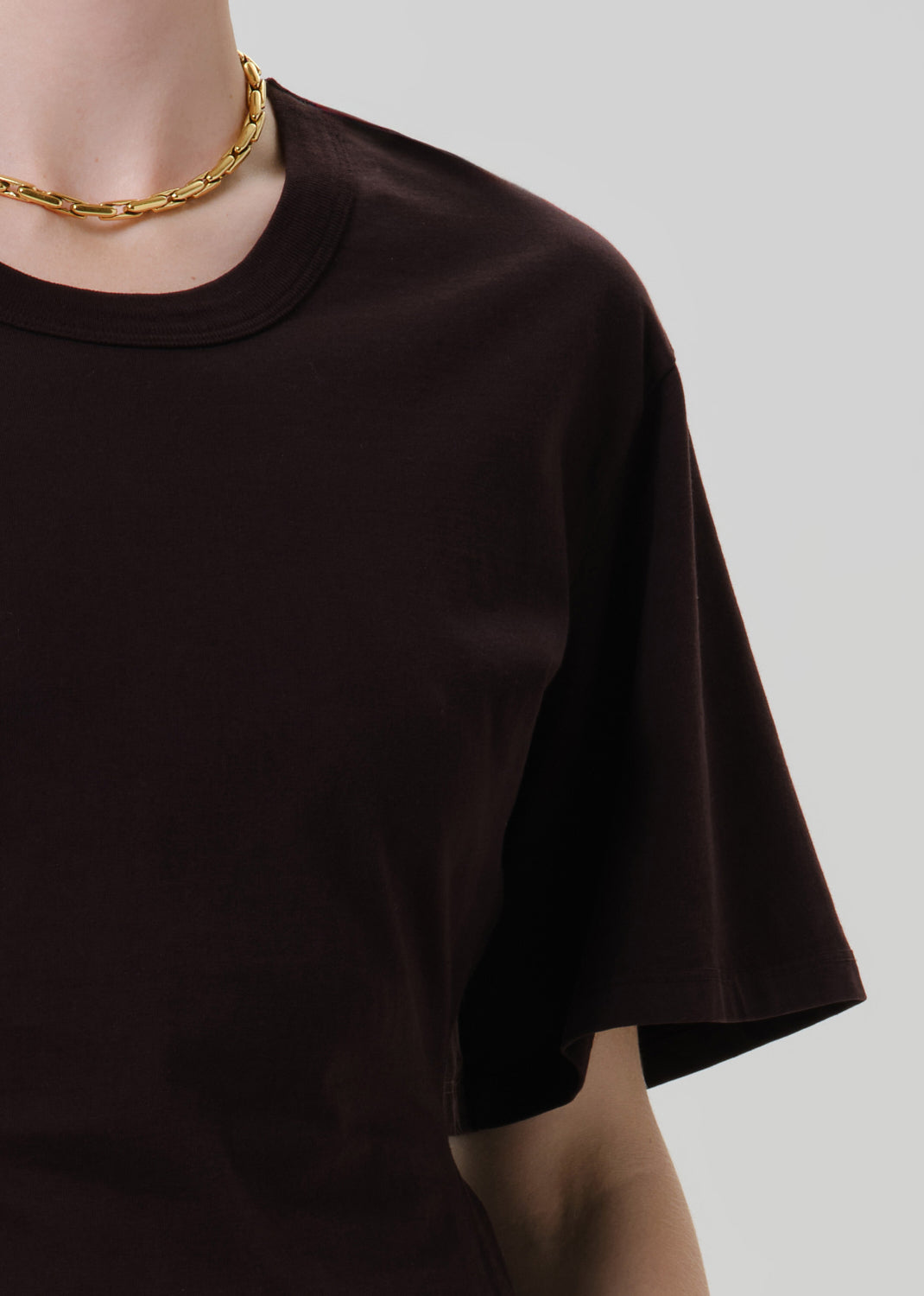 Person wearing a fitted dark brown crewneck short sleeve top on a grey background