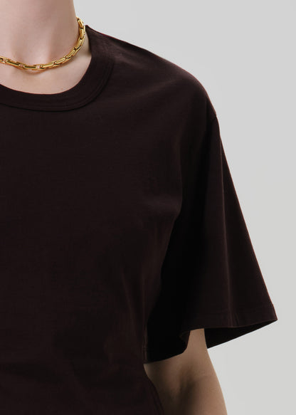 Person wearing a fitted dark brown crewneck short sleeve top on a grey background