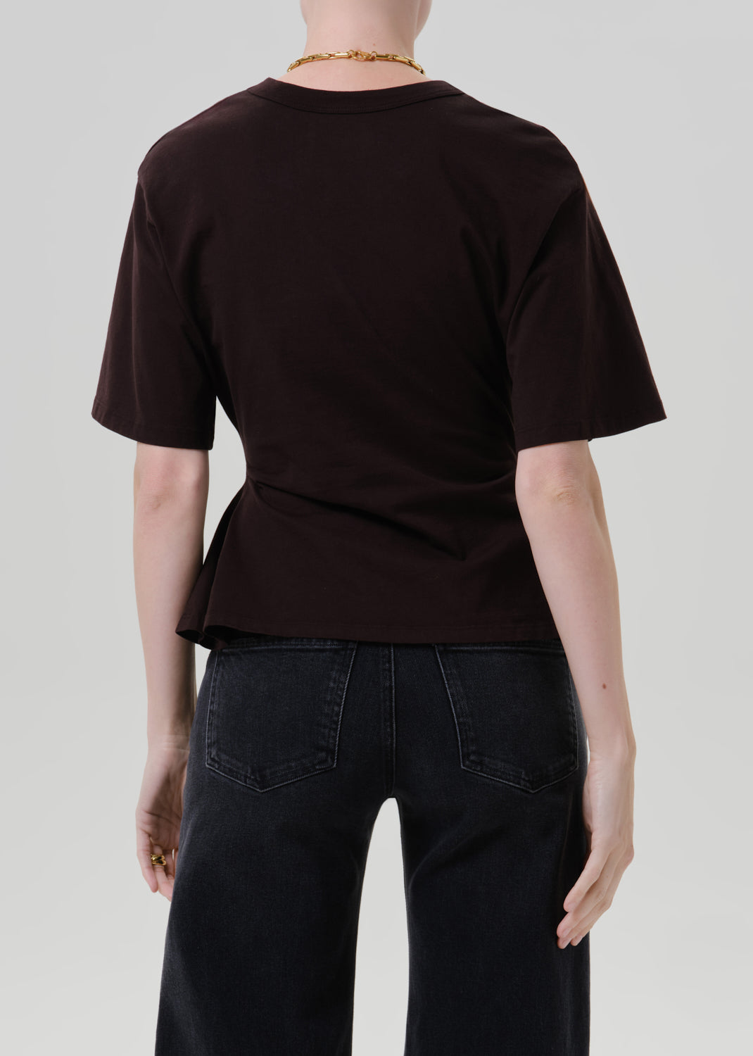 Person wearing a fitted dark brown short sleeve crewneck tee on a grey background