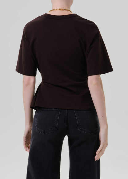Person wearing a fitted dark brown short sleeve crewneck tee on a grey background