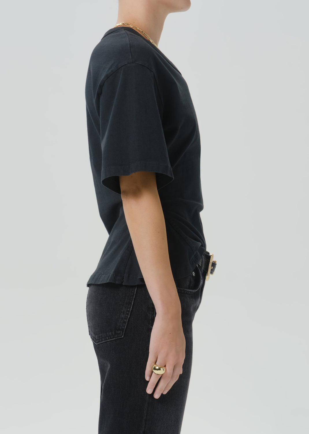 Side profile of a person wearing a black short-sleeve t-shirt and black jeans against a grey background.