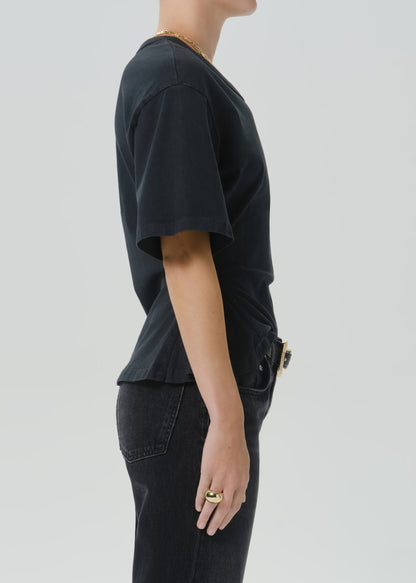 Side profile of a person wearing a black short-sleeve t-shirt and black jeans against a grey background.