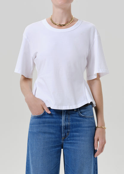 A person wearing a plain white short-sleeve crewneck T-shirt tucked into blue jeans, shown from the neck down against a grey background.