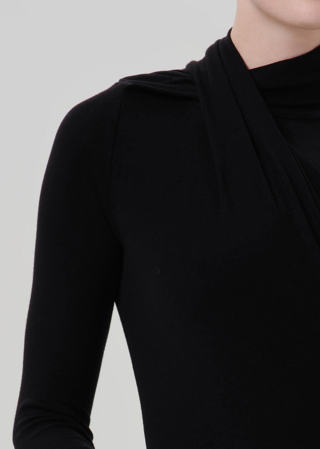 Person wearing a black long sleeve draped mock neck top on a grey background