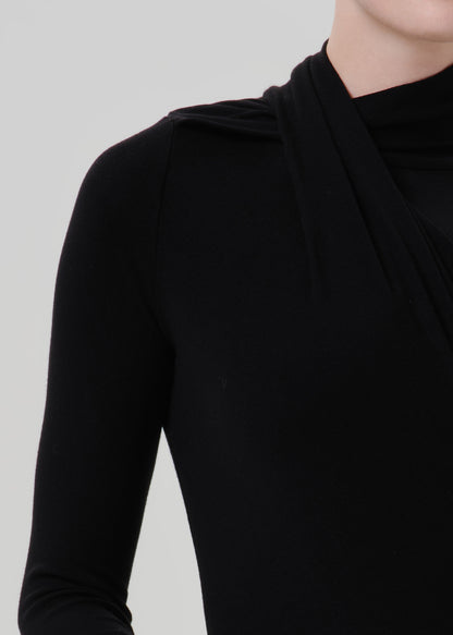 Person wearing a black long sleeve draped mock neck top on a grey background