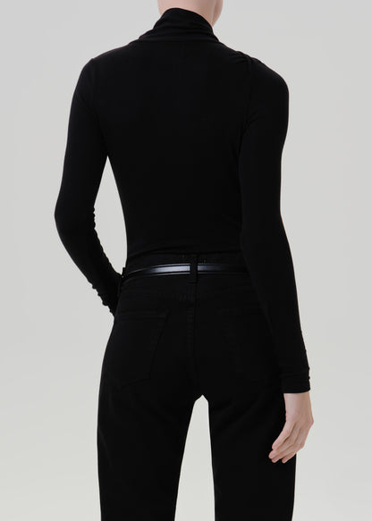 Person wearing a black long sleeve draped mock neck top with black pants viewed from the back on a grey background