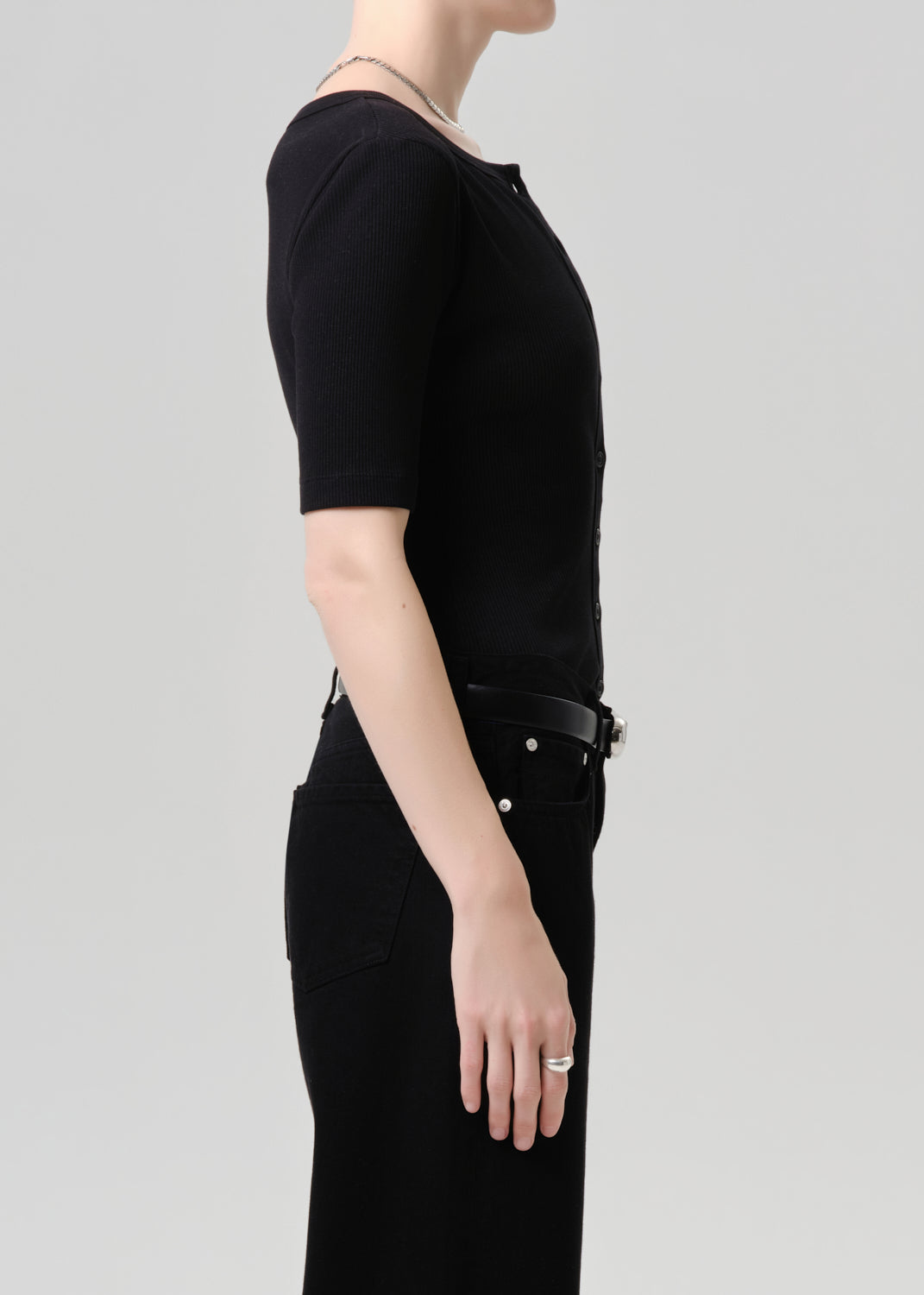 Person wearing a black outfit with a belt on a grey background