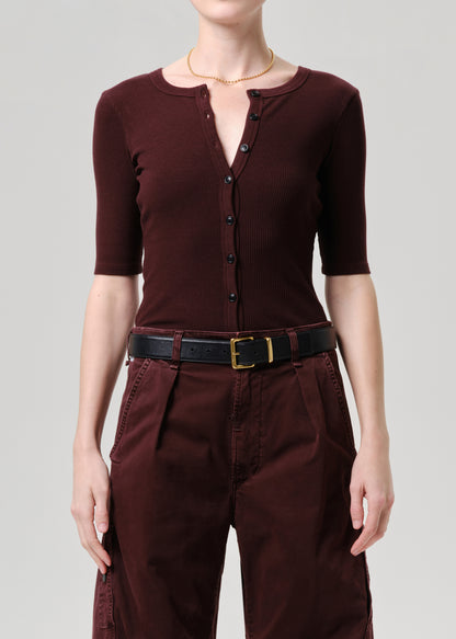 Person wearing a brown outfit with a belt on a grey background