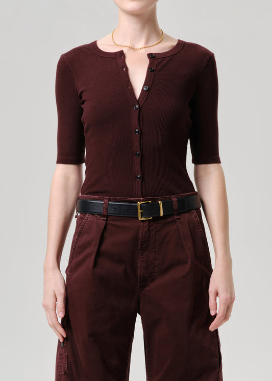 Person wearing a brown outfit with a belt on a grey background