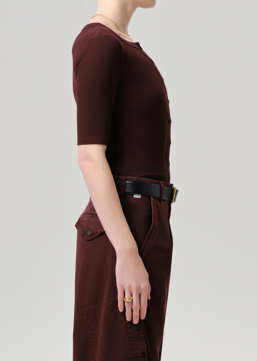 Person wearing a maroon outfit with a belt on a grey background