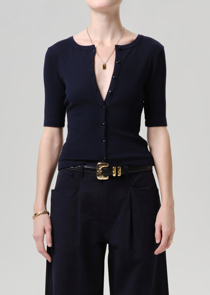 Person wearing a black top and black pants with a gold belt on a grey background