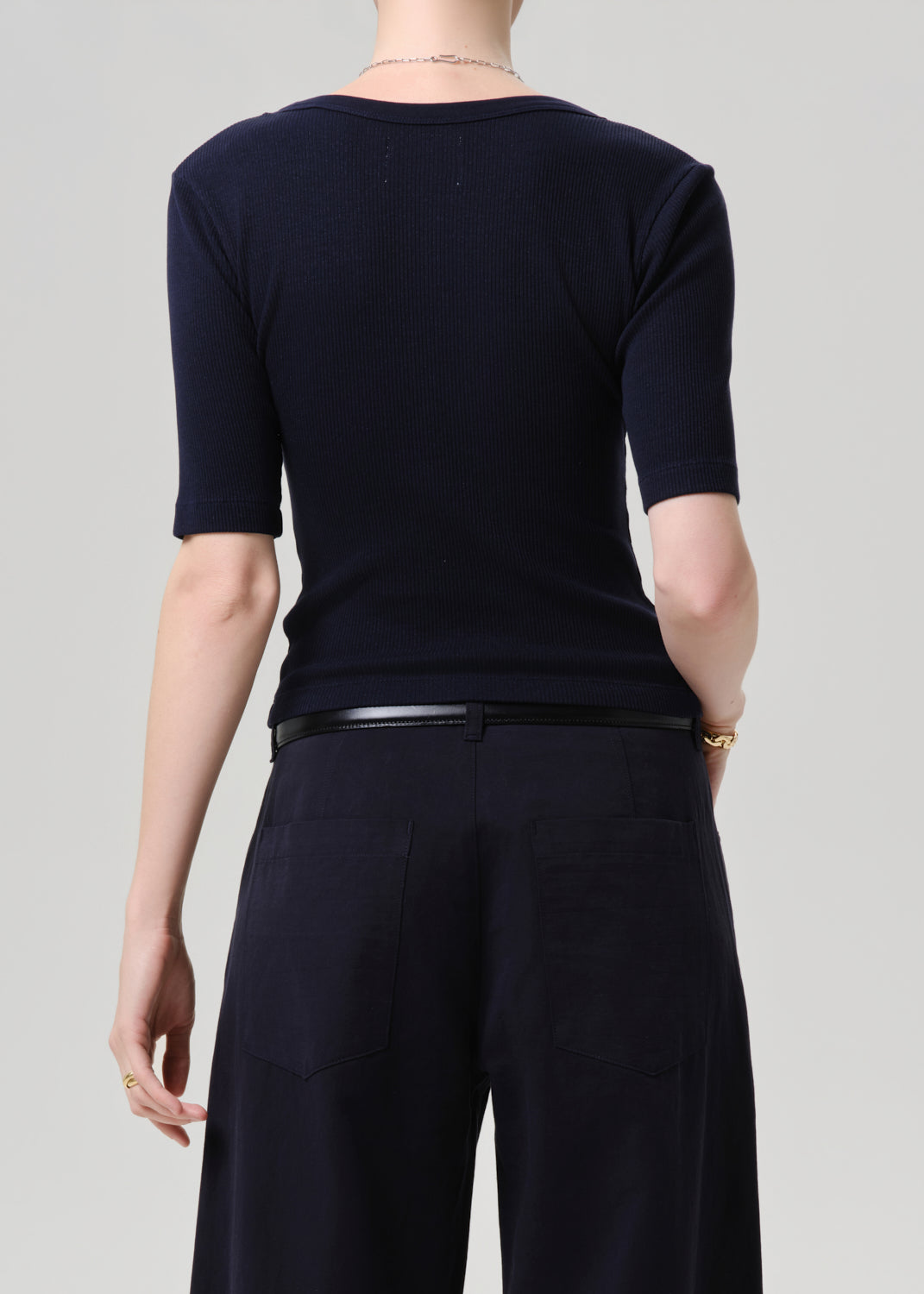 Person wearing a black short-sleeve top and dark pants on a grey background